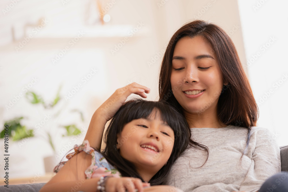 Asian Mum her little daughter hugging sit on sofa smile.Loving family portrait, Mothers Day celebration concept . Asian Mum her little daughter hugging sit on sofa smile.Loving family portrait, Mothers Day celebration concept .