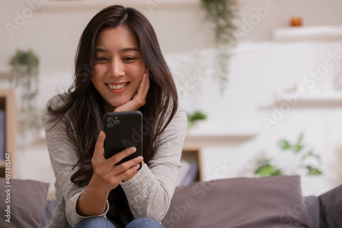 At home, an Asian woman waving a smartphone app enjoys online virtual video chat with pals in a virtual meeting while sharing stories for social media.