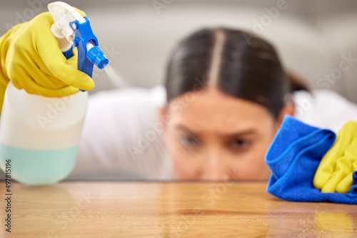 Make sure to be thorough. Shot of a young woman spraying cleaner on her coffee table. photo