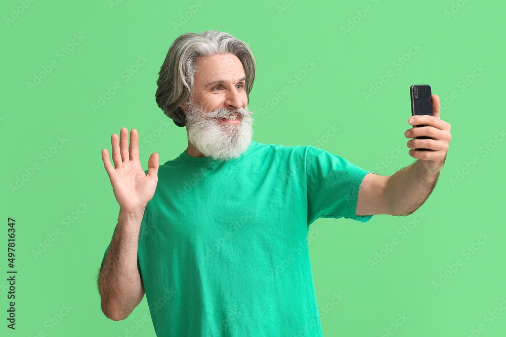 Senior man with mobile phone taking selfie on green background Senior man with mobile phone taking selfie on green background