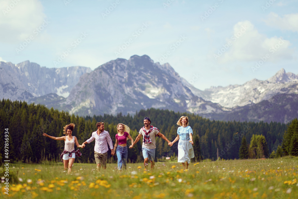 Young friends in casual clothing running through meadow holding hands, enjoying time in nature, summertime. Fun, togetherness, lifestyle, nature concept.