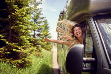 Blonde woman on the window of an rv with hands out smiling enjoying ride. Vacation time. Transport, roadtrip, nature concept.