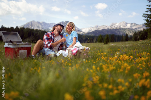 Attractive young couple having picnic in nature. Man giving dandelion flower to woman who is happy. Fun, togetherness, lifestyle, nature concept.