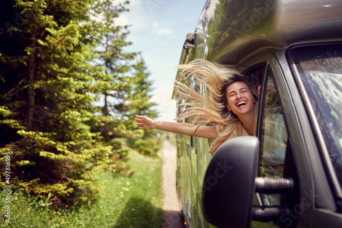 Leinwand Poster Blonde woman on the window of an rv with hands out smiling enjoying ride