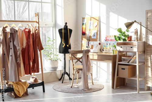 Interior of stylish atelier with tailor's workplace, mannequin and rack photo