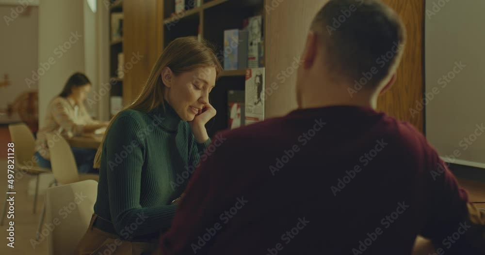 Beautiful woman is sitting at a table with a man in the reading room of the library, a romantic meeting. Young woman is talking to a man in a cozy room. 4k, ProRes Beautiful woman is sitting at a table with a man in the reading room of the library, a romantic meeting. Young woman is talking to a man in a cozy room. 4k, ProRes