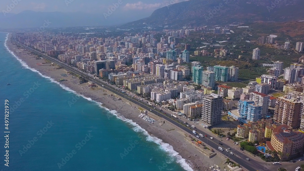 A large city located on a mountain view from a drone. Clip. A resort area near the beach and a huge blue ocean above a bright sky.