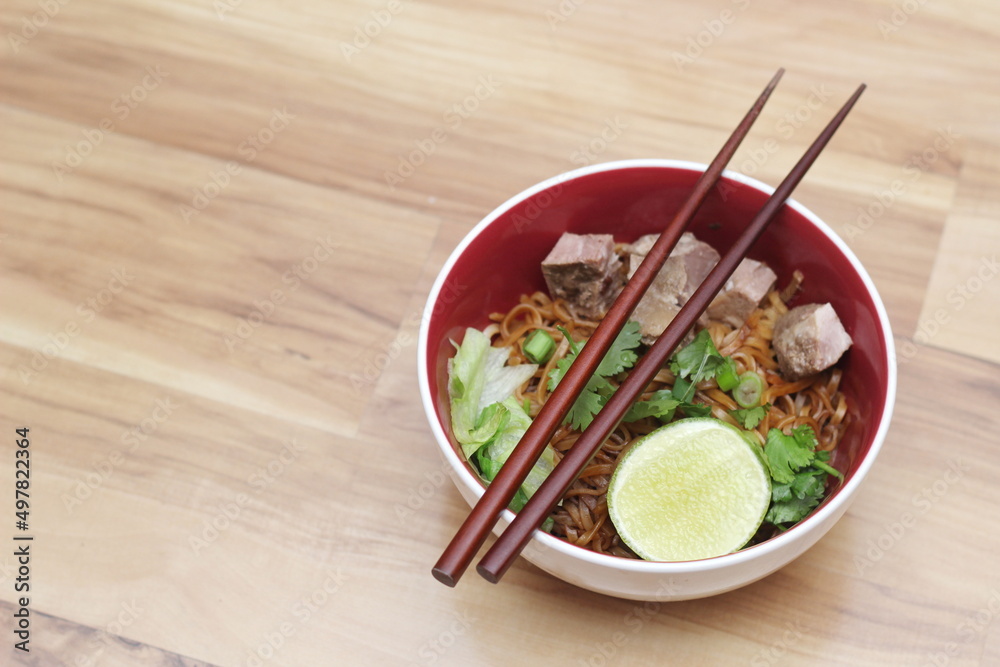 Stewed pork Noodle garnished with coriander, sliced spring onions and lemon wedges. Served on an ash wood table Stewed pork Noodle garnished with coriander, sliced spring onions and lemon wedges. Served on an ash wood table