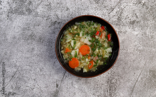 Vegetarian cabbage soup with potatoes, bell peppers, carrots and herbs in bowl on a dark gray background. Top view, flat lay