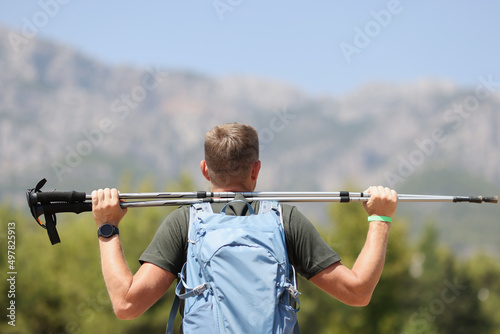Man stands on mountain with back and holds Scandinavian sticks