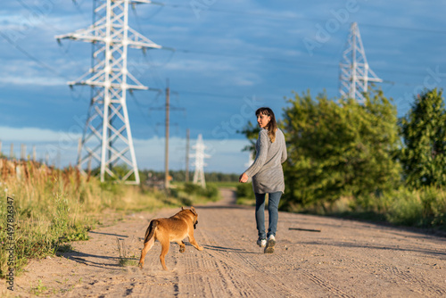 A girl with a dog runs along the road. The girl is photographed in defocus.