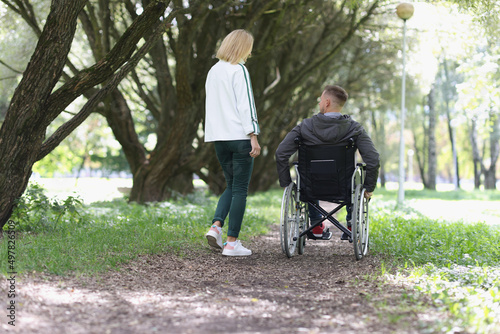 Woman and man in wheelchair are walking in park