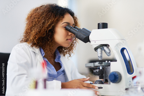 Analysing microscopic data. Cropped shot of a young female scientist looking into a microscope.
