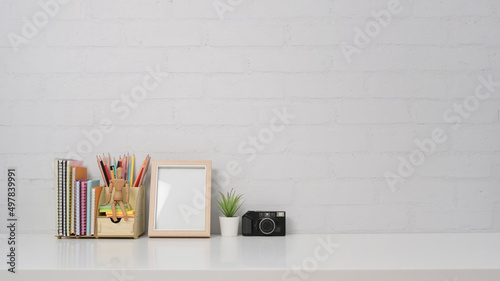 Creative workplace with empty frame, camera and stationery on white table with copy space.