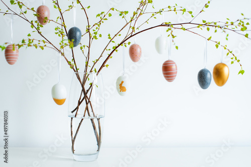 vase with spring branches of blossoming trees, colorful Easter eggs on a white table