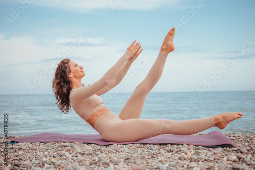 Well looking middle aged woman with black hair  fitness instructor in leggings and tops doing stretching and pilates on yoga mat near the sea. Female fitness yoga routine concept. Healthy lifestyle.