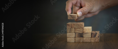 Fotografia Hand is placing wood block tower stack in pyramid stair step with caution to prevent collapse or crash concepts of financial risk management and strategic planning and business challenge plan