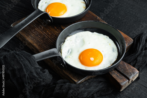 Fried eggs with cherry tomatoe and bread for breakfast in cast iron frying pan, on black wooden table background
