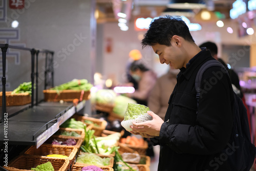 Asian young man picking vegetable in grocery store. Smiling man shopping in supermarket