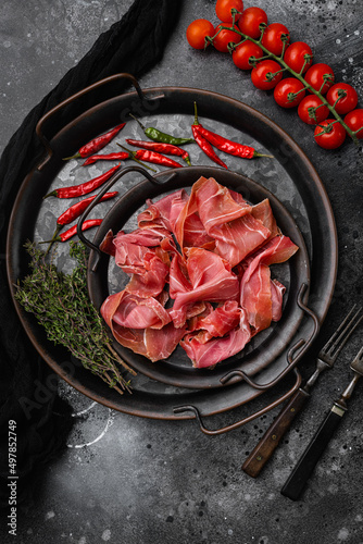 Fresh slices jamon set, on black dark stone table background, top view flat lay, with copy space for text