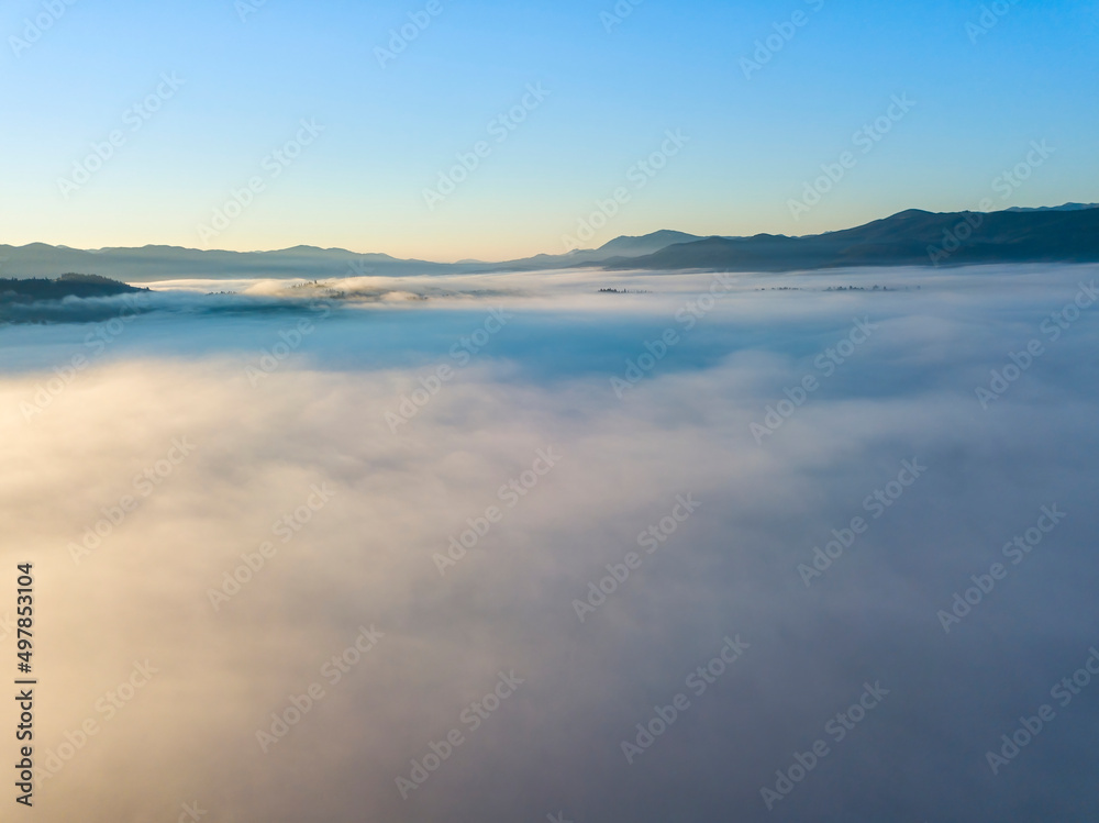 Flight over fog in Ukrainian Carpathians in summer. Mountains on the horizon. A thick layer of fog covers the mountains with a continuous carpet. Aerial drone view.