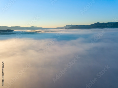 Flight over fog in Ukrainian Carpathians in summer. Mountains on the horizon. A thick layer of fog covers the mountains with a continuous carpet. Aerial drone view.