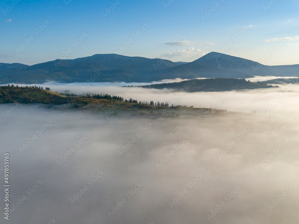 Flight over fog in Ukrainian Carpathians in summer. Mountains on the horizon. A thick layer of fog covers the mountains with a continuous carpet. Aerial drone view.