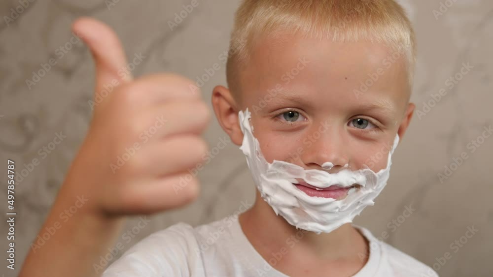 Portrait of a funny little boy with shaving foam on his face in the bathroom, he looks into the camera and gives a thumbs up. Portrait of a funny little boy with shaving foam on his face in the bathroom, he looks into the camera and gives a thumbs up.