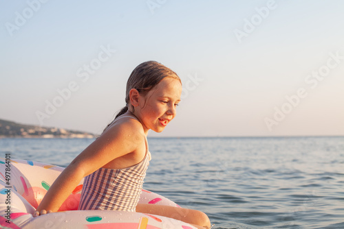 Happy little girl sitting on inflatable ring at tropical beach