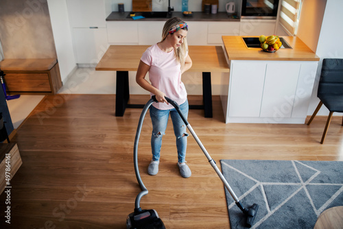 A tired woman vacuuming carpet at home.