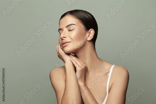 Young female touches her cheeks on light green background