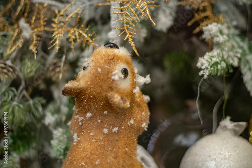Squirrel grabs coniferous branch in winter. Toy squirrel runs through woods. Animal gnaws on twig. Figurine for Christmas.