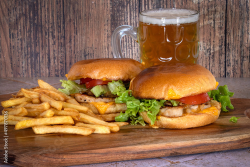 chicken burger with fries on a wooden board with a glass of beer
