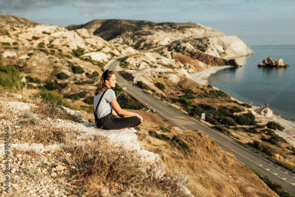 young woman sitting on the ground on the background of the sea coast, sea shore, mountain landscape young woman sitting on the ground on the background of the sea coast, sea shore, mountain landscape