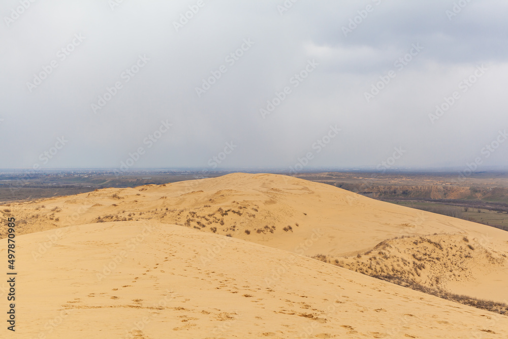 Sarykum dune. Dagestan, Russia. A unique sandy mountain in the Caucasus on a cloudy day. Grass grows on a sand dune. Sarykum dune. Dagestan, Russia. A unique sandy mountain in the Caucasus on a cloudy day. Grass grows on a sand dune.