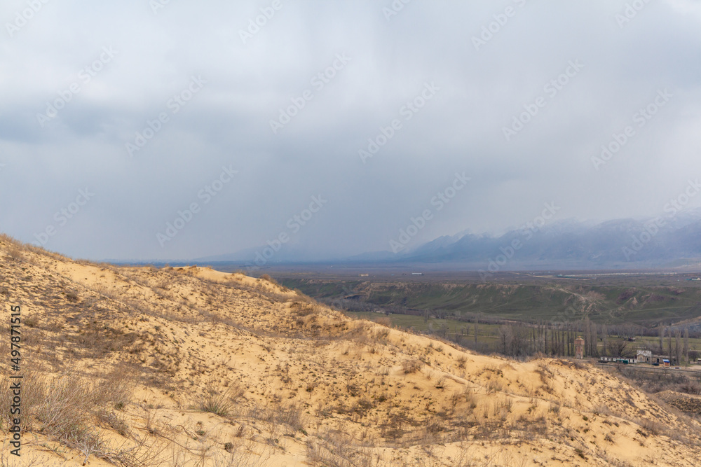 Sarykum dune. Dagestan, Russia. A unique sandy mountain in the Caucasus on a cloudy day. Grass grows on a sand dune. Sarykum dune. Dagestan, Russia. A unique sandy mountain in the Caucasus on a cloudy day. Grass grows on a sand dune.