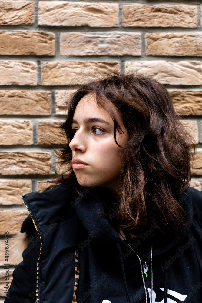 Portrait of teenager turkish girl in front of bricks wall. Black wearing teen looking aside