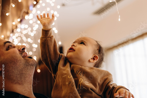 Father and son playing with lights garland. Dad holds his baby boy on arms