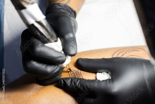 Hands of tattoo artist in black gloves busy with work at tattoo shop. 
