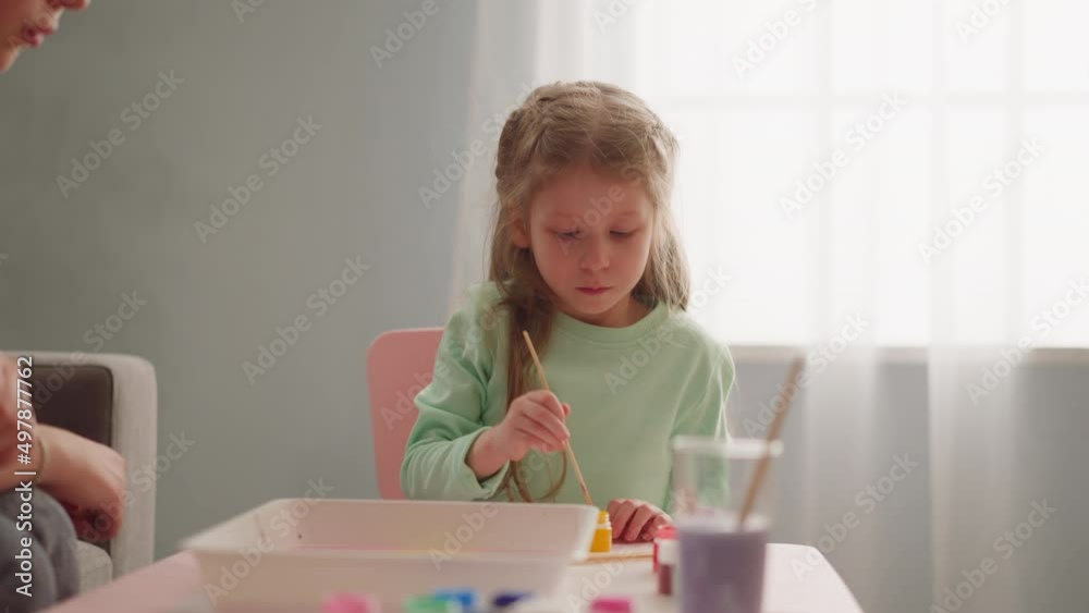 Serious little girl draws Ebru art with yellow paint and stick with sister at workshop in living room slow motion. Development hobby for kids Serious little girl draws Ebru art with yellow paint and stick with sister at workshop in living room slow motion. Development hobby for kids
