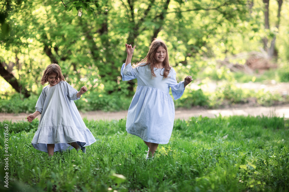 Happy funny children are spinning in the meadow in the park, girls in beautiful dresses hold hands and play in the tall grass. Happy childhood and spring. Happy funny children are spinning in the meadow in the park, girls in beautiful dresses hold hands and play in the tall grass. Happy childhood and spring.