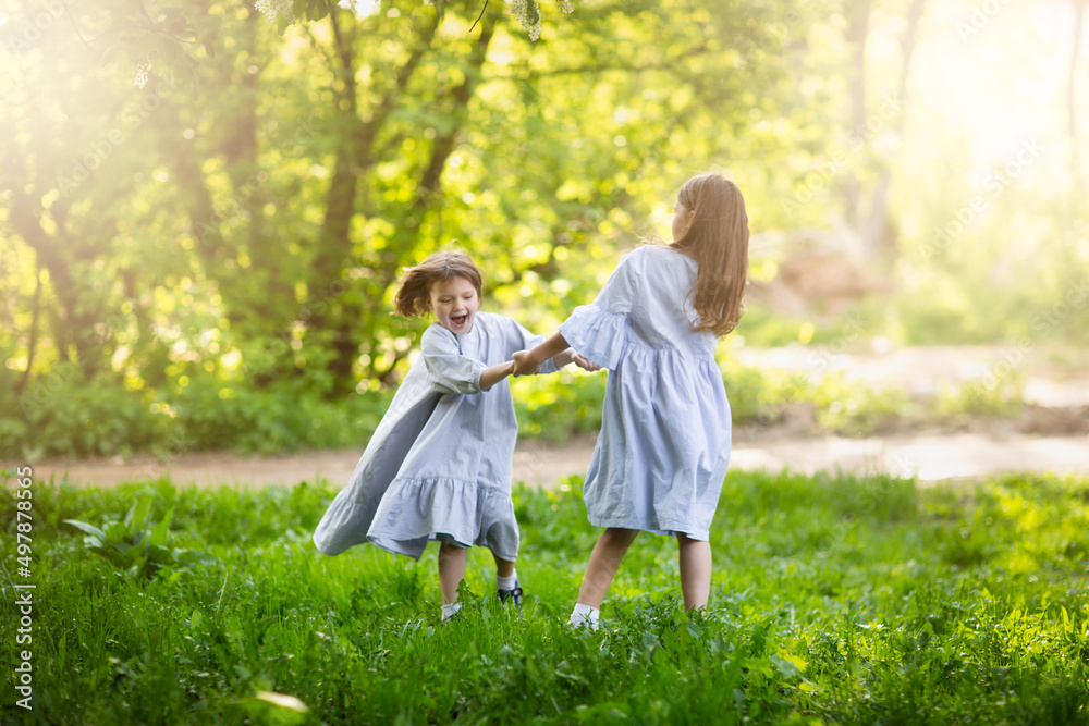 Happy funny children are spinning in the meadow in the park, girls in beautiful dresses hold hands and play in the tall grass. Happy childhood and spring. Happy funny children are spinning in the meadow in the park, girls in beautiful dresses hold hands and play in the tall grass. Happy childhood and spring.