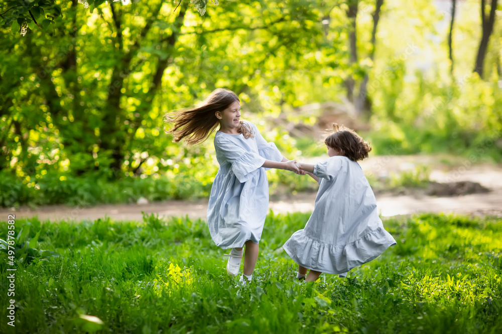 Happy funny children are spinning in the meadow in the park, girls in beautiful dresses hold hands and play in the tall grass. Happy childhood and spring. Happy funny children are spinning in the meadow in the park, girls in beautiful dresses hold hands and play in the tall grass. Happy childhood and spring.