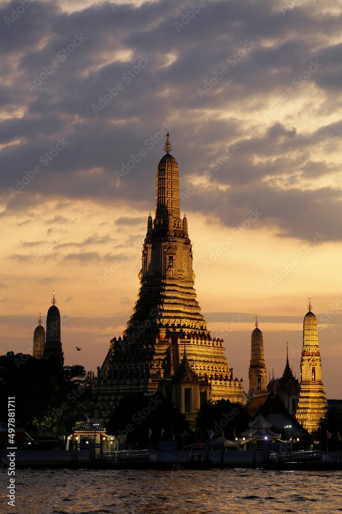 The sun sets near the Wat Arun Buddhist temple located in the bank of Chao Phraya river, Bangkok, Thailand.
