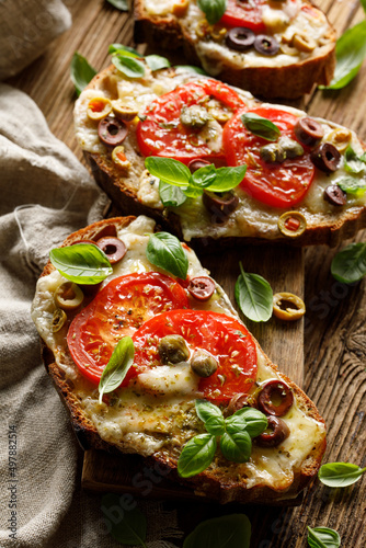 Grilled sandwiches, bruschettes made of sourdough bread with the addition of cheese, tomatoes and olives sprinkled with herbs, close up view