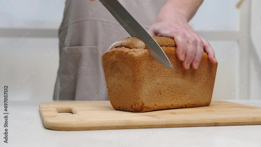 Man cutting loaf of rye black bread with knife on wooden board on table in kitchen close-up. Man cutting loaf of rye black bread with knife on wooden board on table in kitchen close-up.
