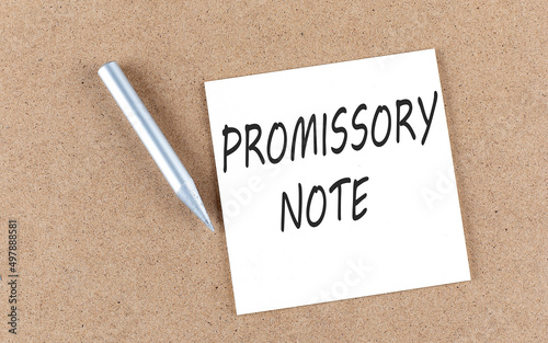 PROMISSORY NOTE text on sticky note on a cork board with pencil , photo