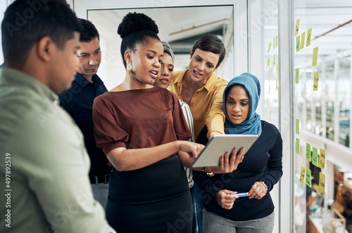 Technology helps them better understand their big plans. Shot of a group of businesspeople using a digital tablet while brainstorming with notes on a glass wall in an office.