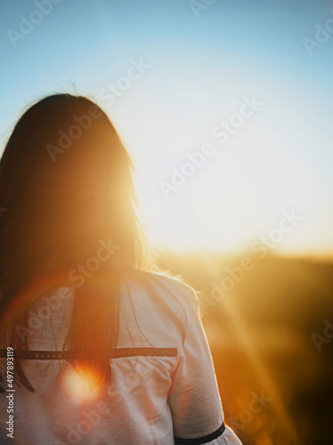 Blurred woman in an embroidered shirt stands with her back to the sunset. Support for Ukraine.