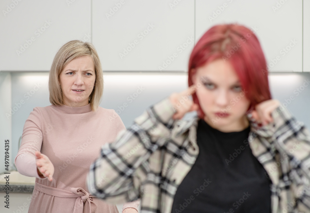 Angry mother scolds her teen daughter. Girl covers her ears and ignores her mother. Family relationships concept